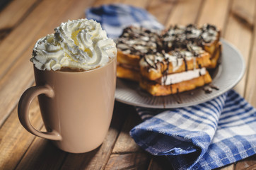 waffles with cream and chocolate on the plate and coffee on a wooden table.