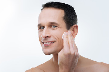 Obraz premium Looking good. Portrait of a handsome delighted man using a cotton pad while cleaning his skin
