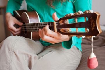 Fototapeta na wymiar Young man's hands playing an acoustic guitar ukulele at the home. A man playing ukulele in close up view.