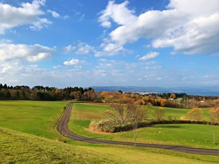 Fototapeta na wymiar A small road and the grass field with sky and cloud with horizon. A rural parking area near Hakodate, Hokkaido, Japan