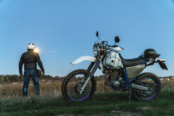 Obraz na płótnie Canvas Active way of life, enduro motorcycle, a guy looks at the stars at night and the moon, unity with nature, the spirit of adventure, escape from the hustle and bustle of the city, travel concept