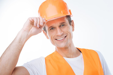 Successful career. Portrait of a delighted happy nice engineer smiling and touching his helmet while thinking about his safety