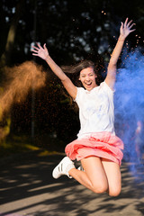 Fototapeta na wymiar Expressive brunette asian woman jumping with Holi paint exploding around her