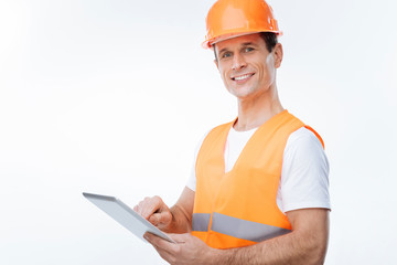 Safety equipment. Positive happy nice engineer smiling and toughing his helmet while carrying his draughts