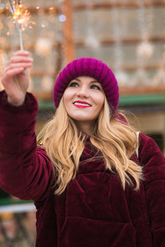 Cool blonde girl dressed in stylish clothes, holding glowing sparklers at the Christmas fair in Kiev