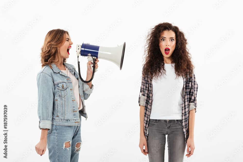 Poster shocked curly woman covering her ears while second girl screaming