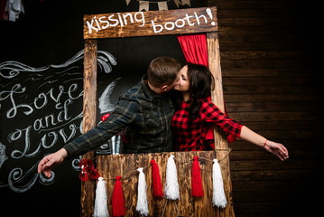 Young cheerful european couple in love embracing in kissing booth, in decorated with hearts studio on valentine day, dating.