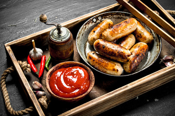 Sausages in a frying pan with sauce on a wooden tray.