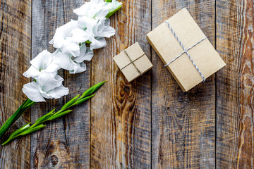 Gift box wrapped in craft paper near flower gladiolus on wooden 