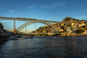 View of the Dom Luis bridge from the bank of the Douro River in Porto, Portugal, during a summer afternoon.