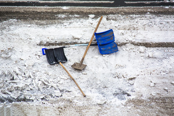 Plastic snow shovel in a snow bank on pavement.