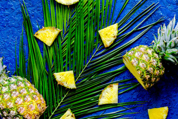 Pineapple and palm branch on blue table background top view
