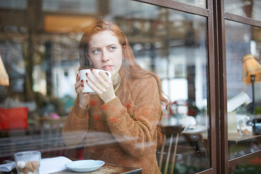 View through window of woman in coffee shop holding cup