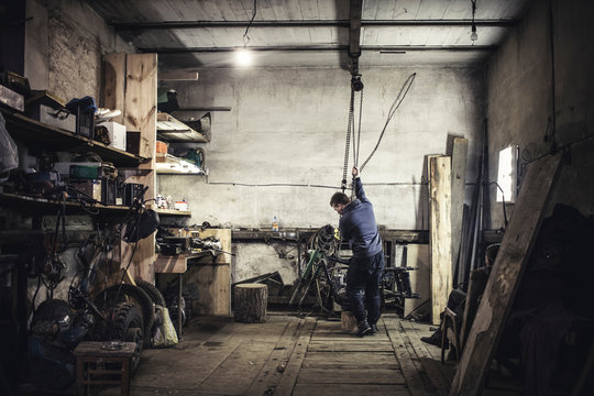 Mechanic hoisting dismantled vintage motorcycle in workshop