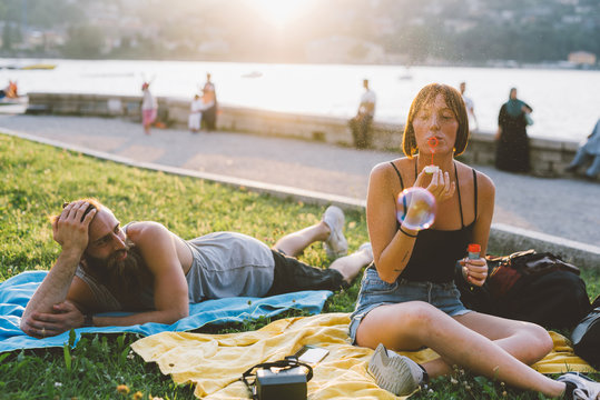 Young couple blowing bubbles on waterfront grass, Lake Como, Lombardy, Italy