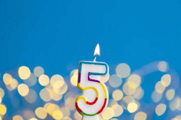 Number 5 birthday celebration candle against a bright lights and blue background