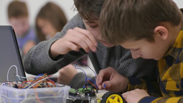 Two boy classmates constructing bot car with wires and light at practical lesson