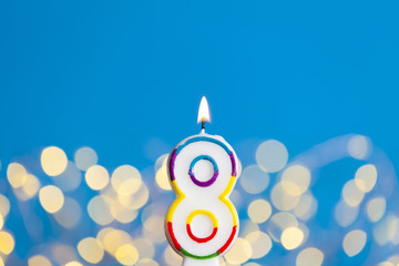 Number 8 birthday celebration candle against a bright lights and blue background