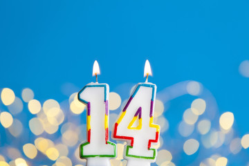 Number 14 birthday celebration candle against a bright lights and blue background