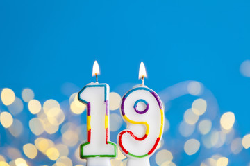Number 19 birthday celebration candle against a bright lights and blue background