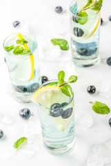 Summer refreshment drinks, Blueberry Lemonade or mojito cocktail with lemon, fresh blueberries and mint, white marble background copy space