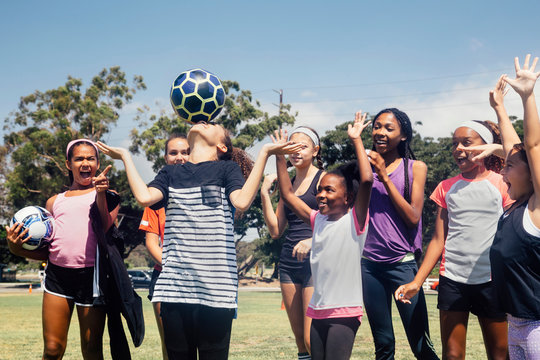 Schoolgirl soccer team watching player balancing soccer ball on nose on school sports field