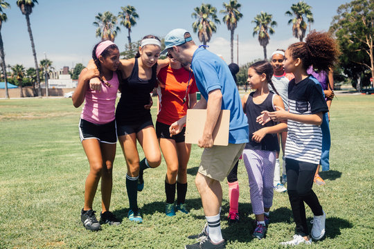 Schoolgirl soccer team and teacher supporting injured player on school sports field