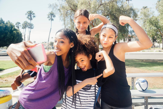 Schoolgirl soccer players taking smartphone selfie on school sports field - Powered by Adobe