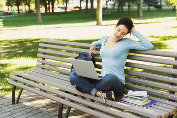 Happy relaxed young woman using laptop in park