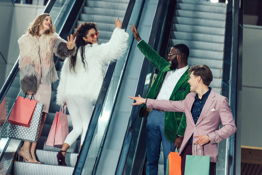 Young Male And Female Shoppers Giving High Five On Escalators At Mall