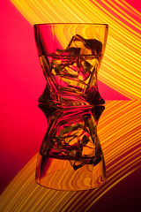 Cocktail whiskey a glass with pieces ice of party reflection a concept of hourglasses yellow light effects on red background.