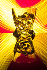 Cocktail whiskey a glass with pieces ice of party reflection a concept of hourglasses yellow light effects on red background.
