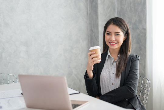 Asian business girl in her workstation at holding coffee cup and smile