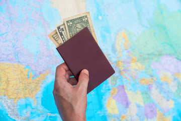Hand holding a passport with blank and dollars with a world map in background