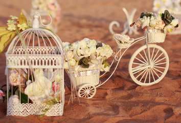 Wedding ceremony objects, signs, symbols, attributes and accessories. Flowers, white roses bouquet bunch, small beautiful cage and toy bicycle on sandy beach as ceremony decoration elements