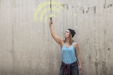 Woman holding up phone looking for signal with wifi sign drawn in yellow chalk on concrete wall