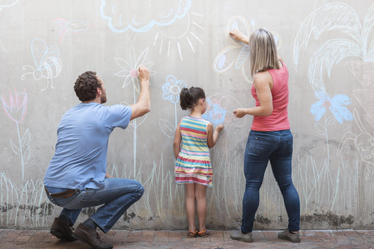 Family drawing colorful pictures with chalk on a concrete wall