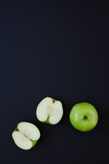 Green apple and two halves of apple on black background