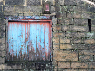 boarded window with decaying blue painted shutters with rotting wood in a derelict abandoned house...