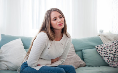 Woman suffering from abdominal pain while sitting on sofa at home