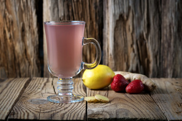 warming ginger drink with raspberries and lemon with a tall glass Cup on a wooden table