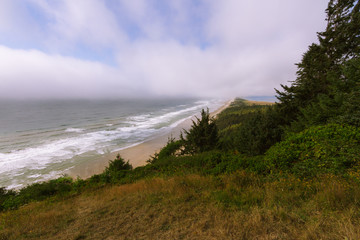 Viewpoint above sand beach and crashing waves near Netarts Bay in clouds in Oregon, USA