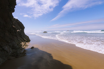 Crashing waves on empty beach with cliffs in fog during sunny day on Hug Point, Oregon, USA