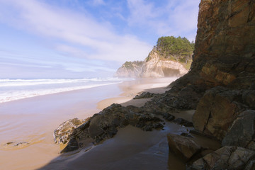 Crashing waves on empty beach with cliffs in fog during sunny day on Hug Point, Oregon, USA