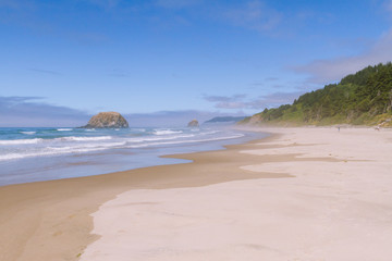 Fototapeta na wymiar Crashing waves on empty beach with cliffs in fog during sunny day on Hug Point, Oregon, USA