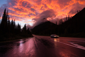 Car on highway with reflections  in Canada surrounded by mountains in clouds during orange sunset - 187617603