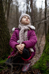 Little girl sitting near a tree in an autumn forest