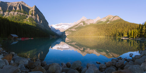 Fototapeta na wymiar Cabin with canoe and reflection on Lake Louise in Rocky Mountains in Canada during sunrise on sunny day