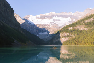 Fototapeta premium People on canoe on Lake Louise with reflection on water in Rocky Mountains in Canada during sunrise on sunny day