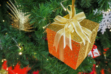 Golden christmas box hanging on Christmas tree.